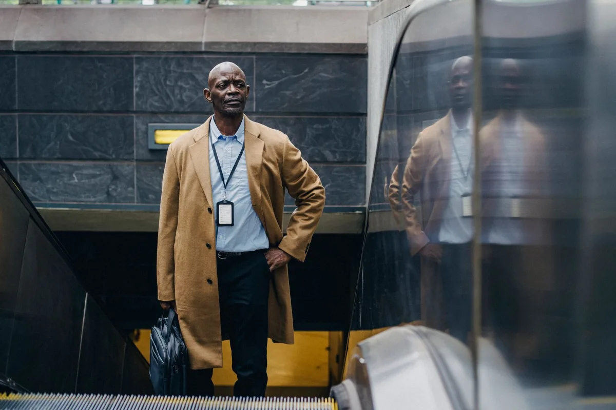 Confident adult African American businessman in formal clothes riding escalator with hand in pocket while leaving metro station and looking away thoughtfully Confident adult African American businessman in formal clothes riding escalator with hand in pocket while leaving metro station and looking away thoughtfully
