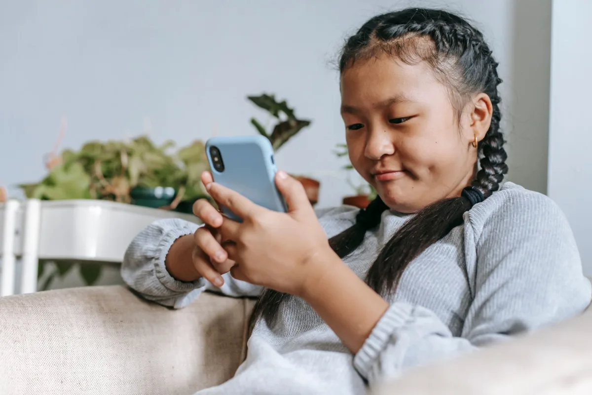 Focused ethnic girl in casual outfit sitting on comfortable armchair and browsing internet on smartphone Focused ethnic girl in casual outfit sitting on comfortable armchair and browsing internet on smartphone