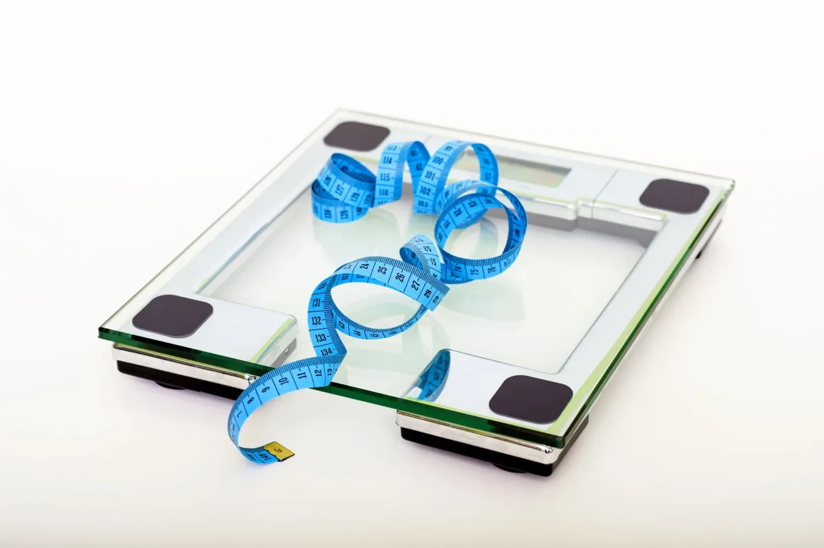 A digital glass weighing scale with a blue tape, symbolizing weight management. A digital glass weighing scale with a blue tape, symbolizing weight management.