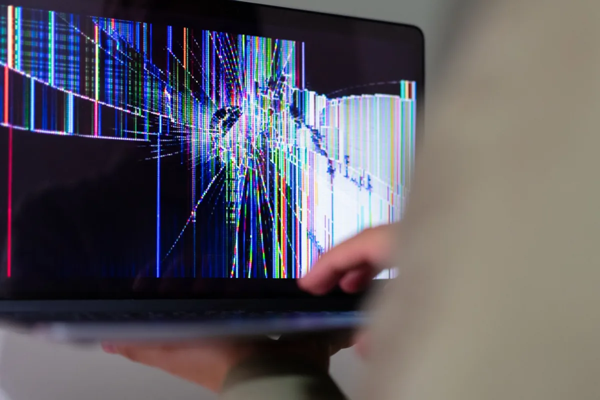 A close-up view of a cracked laptop screen displaying colorful digital distortion. A close-up view of a cracked laptop screen displaying colorful digital distortion.
