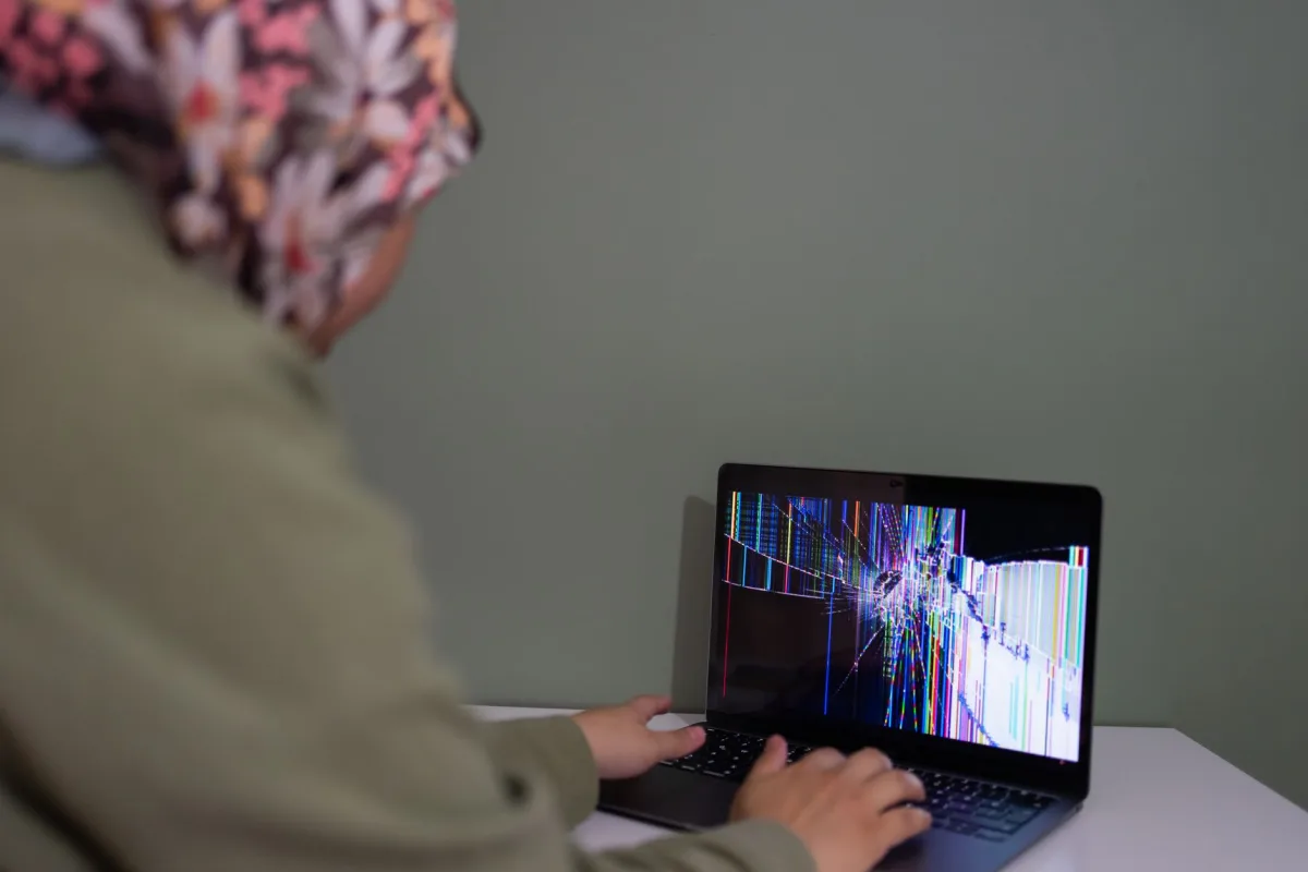 A person interacts with a laptop displaying a colorful cracked screen indoors. A person interacts with a laptop displaying a colorful cracked screen indoors.