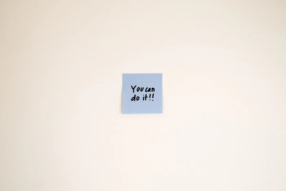 A motivational on a blue Post-it note reads 'You can do it!' on a cream wall.