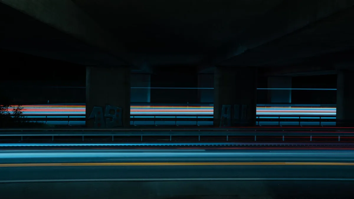 Long exposure shot capturing colorful light trails on a city road under a bridge at night.