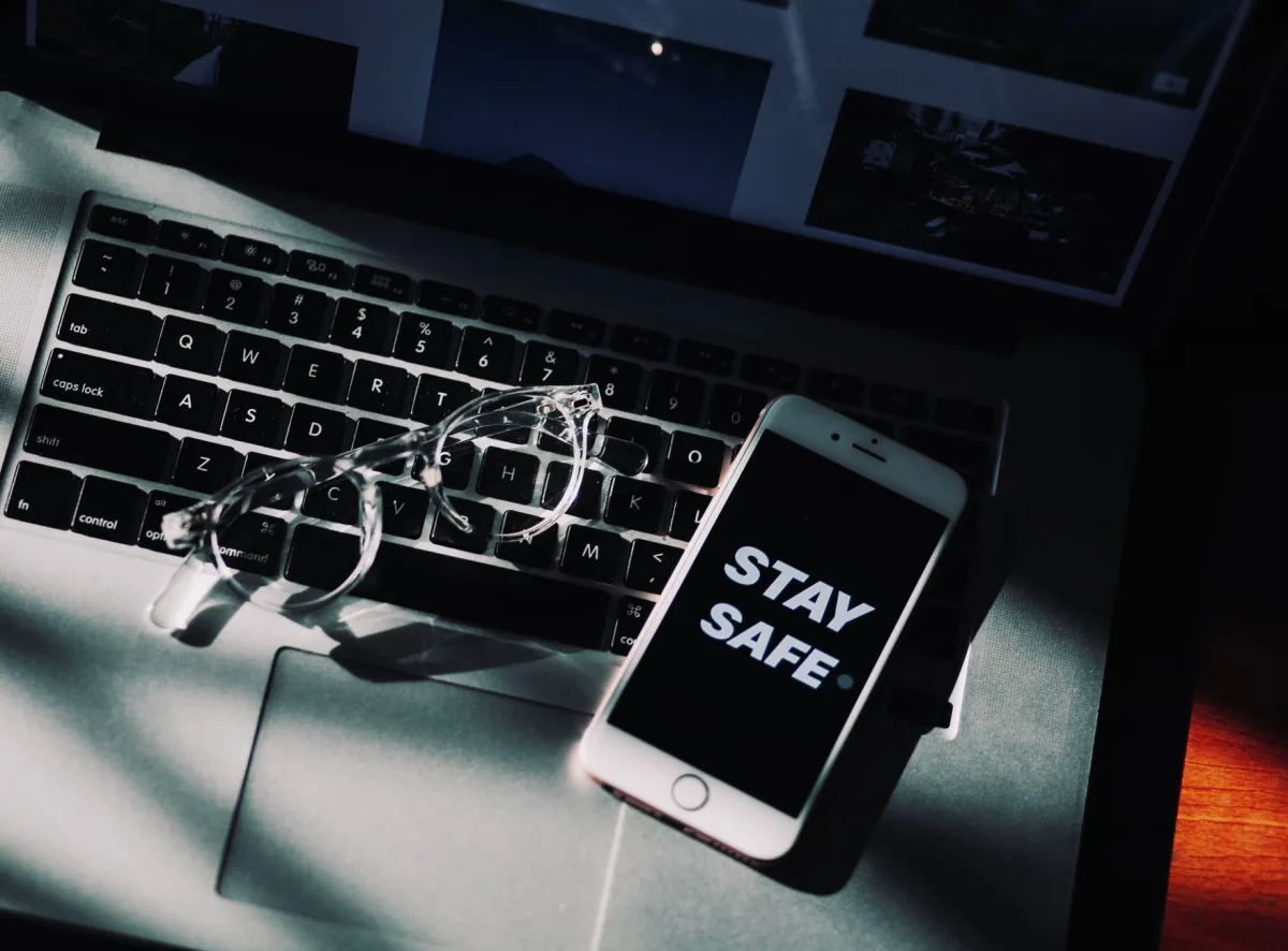 Eyeglasses and smartphone display 'Stay Safe' on laptop, emphasizing remote work.