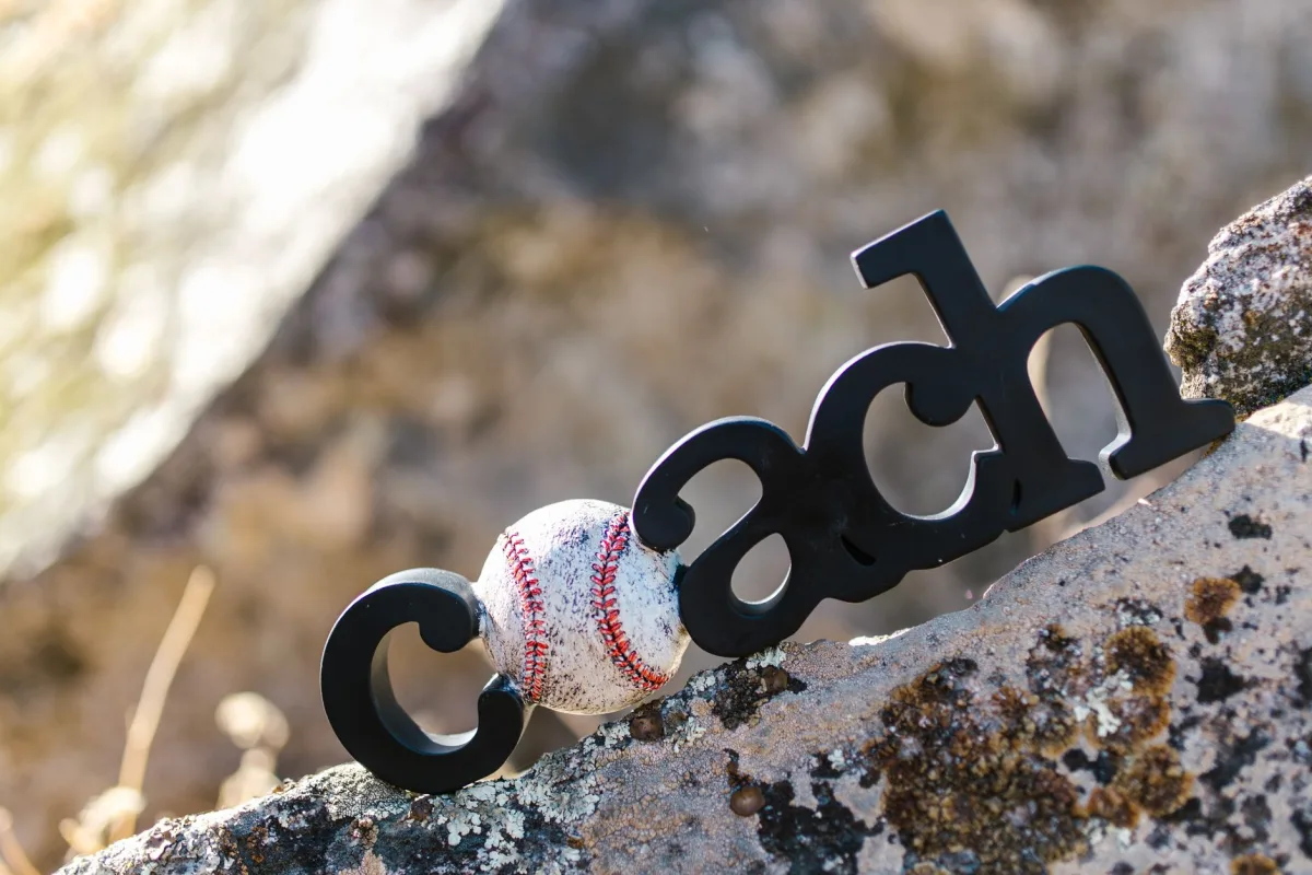 A baseball resting against a 'coach' sign on a rocky surface, outdoors.