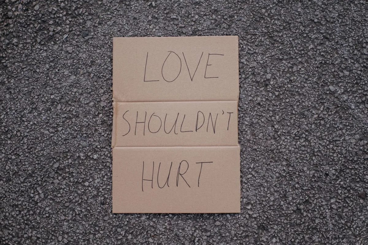 Top view of social slogan love should not hurt on cardboard placed on asphalt road on urban street