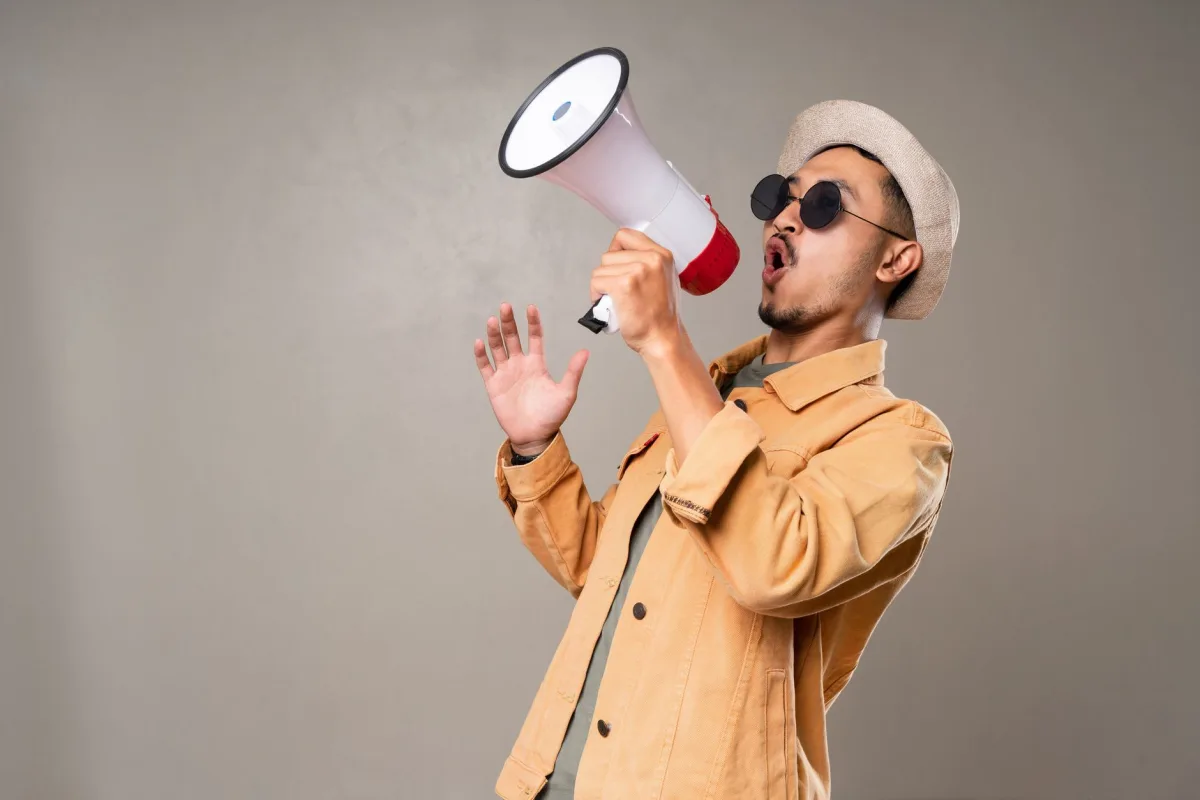 Man with sunglasses and hat energetically shouting into a megaphone indoors. Man with sunglasses and hat energetically shouting into a megaphone indoors.