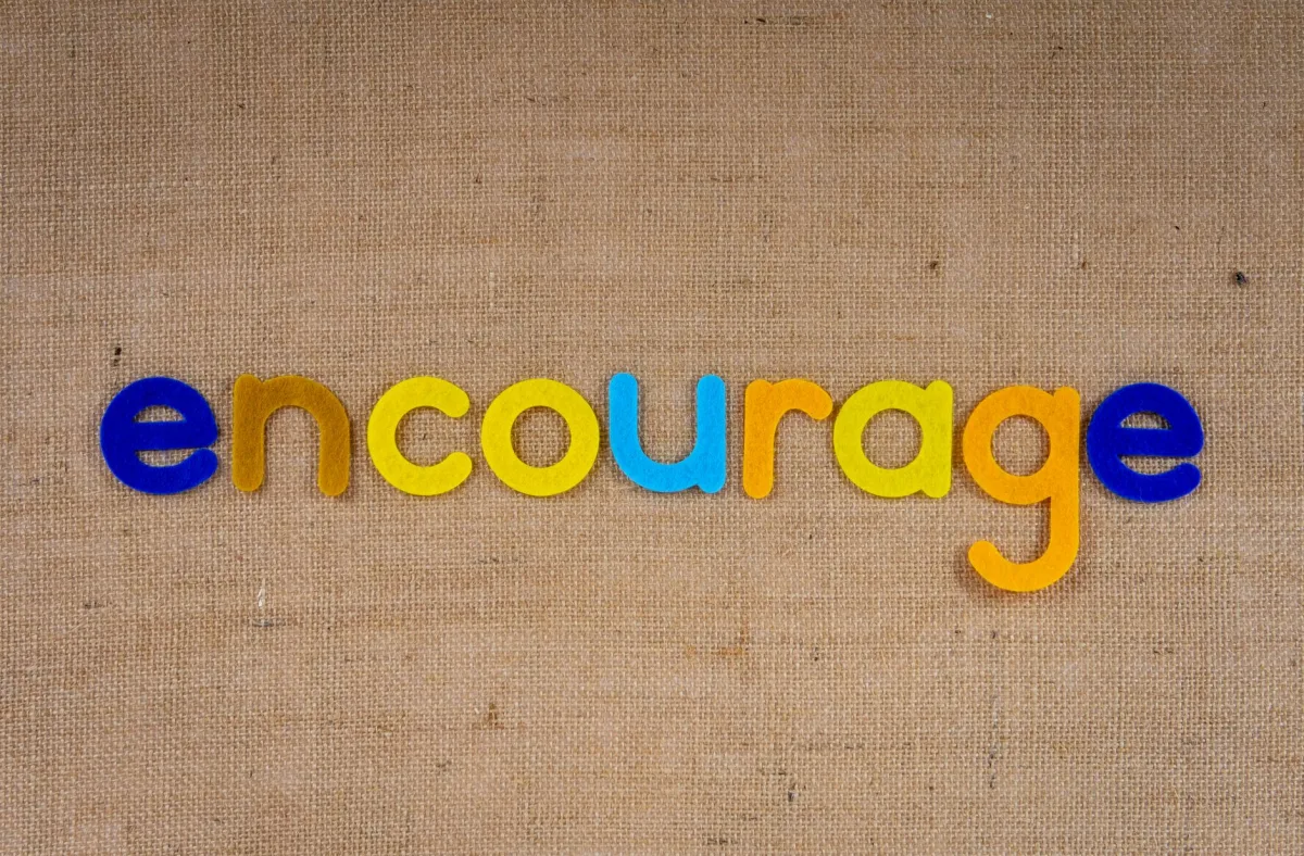 The word 'encourage' in colorful letters on a brown burlap texture, conveying positivity and motivation. The word 'encourage' in colorful letters on a brown burlap texture, conveying positivity and motivation.