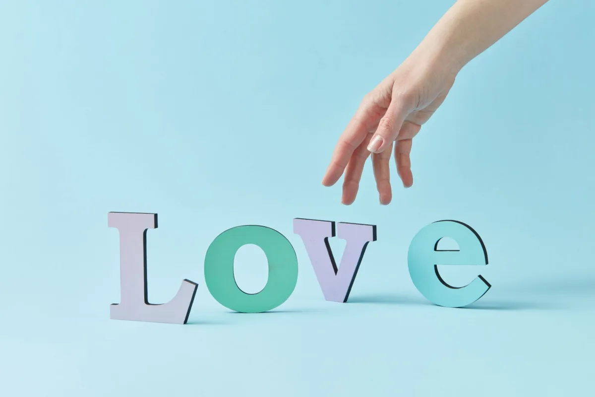 A hand reaches for colorful letters spelling 'Love' on a blue background, symbolizing connection and emotion. A hand reaches for colorful letters spelling 'Love' on a blue background, symbolizing connection and emotion.