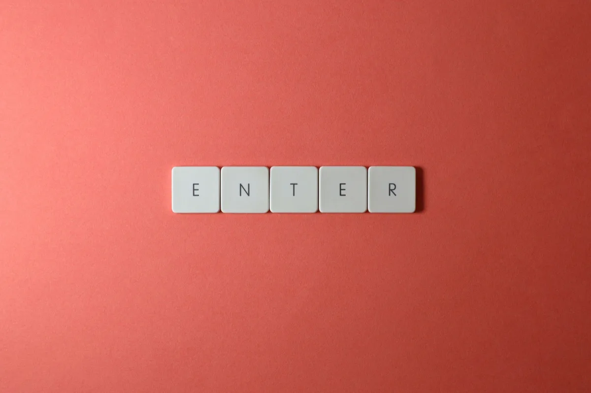 Close-up of five keyboard letter tiles spelling 'ENTER', placed on a coral backdrop. Close-up of five keyboard letter tiles spelling 'ENTER', placed on a coral backdrop.