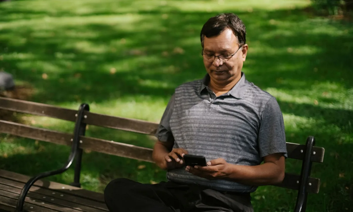 Ethnic male in casual outfit using smartphone while sitting on bench on park Ethnic male in casual outfit using smartphone while sitting on bench on park