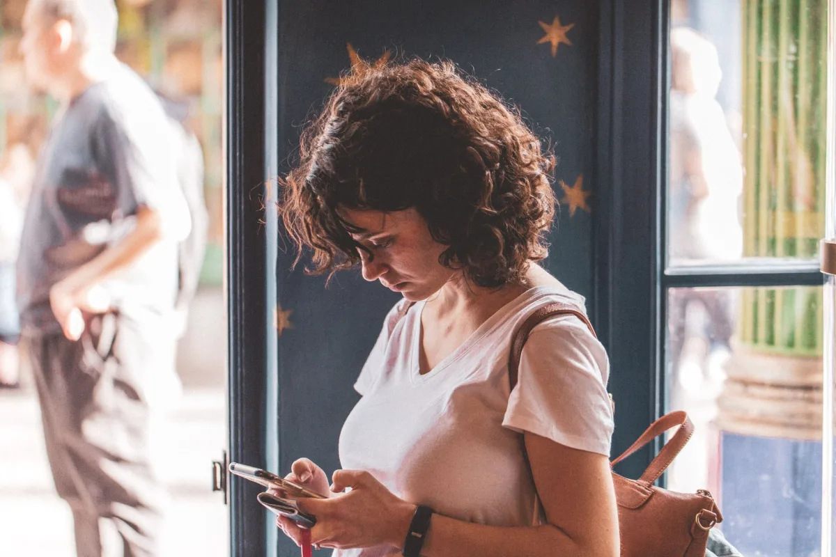 Woman with curly hair using smartphone by a sunlit window, wearing a white t-shirt. Woman with curly hair using smartphone by a sunlit window, wearing a white t-shirt.