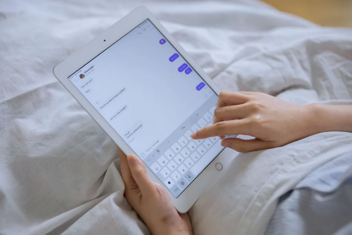 Close-up of hands typing on a digital tablet with messaging app in bed. Close-up of hands typing on a digital tablet with messaging app in bed.