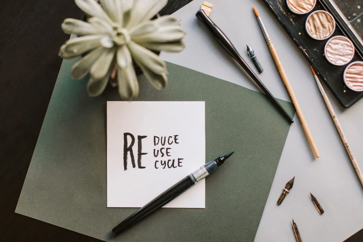 Flat lay of art materials featuring a recycle-themed note and calligraphy tools. Flat lay of art materials featuring a recycle-themed note and calligraphy tools.