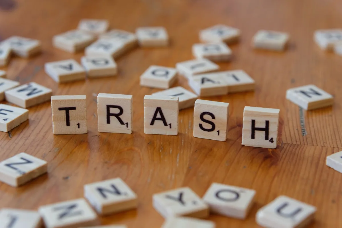 Arrangement of wooden letter tiles spelling trash on a wooden table surface.