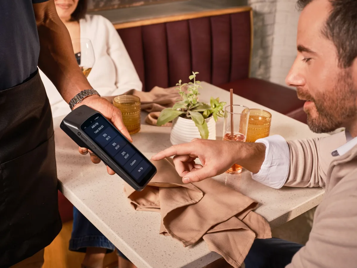 A diner uses a handheld POS system digital tipping in a casual restaurant setting. A diner uses a handheld POS system digital tipping in a casual restaurant setting.