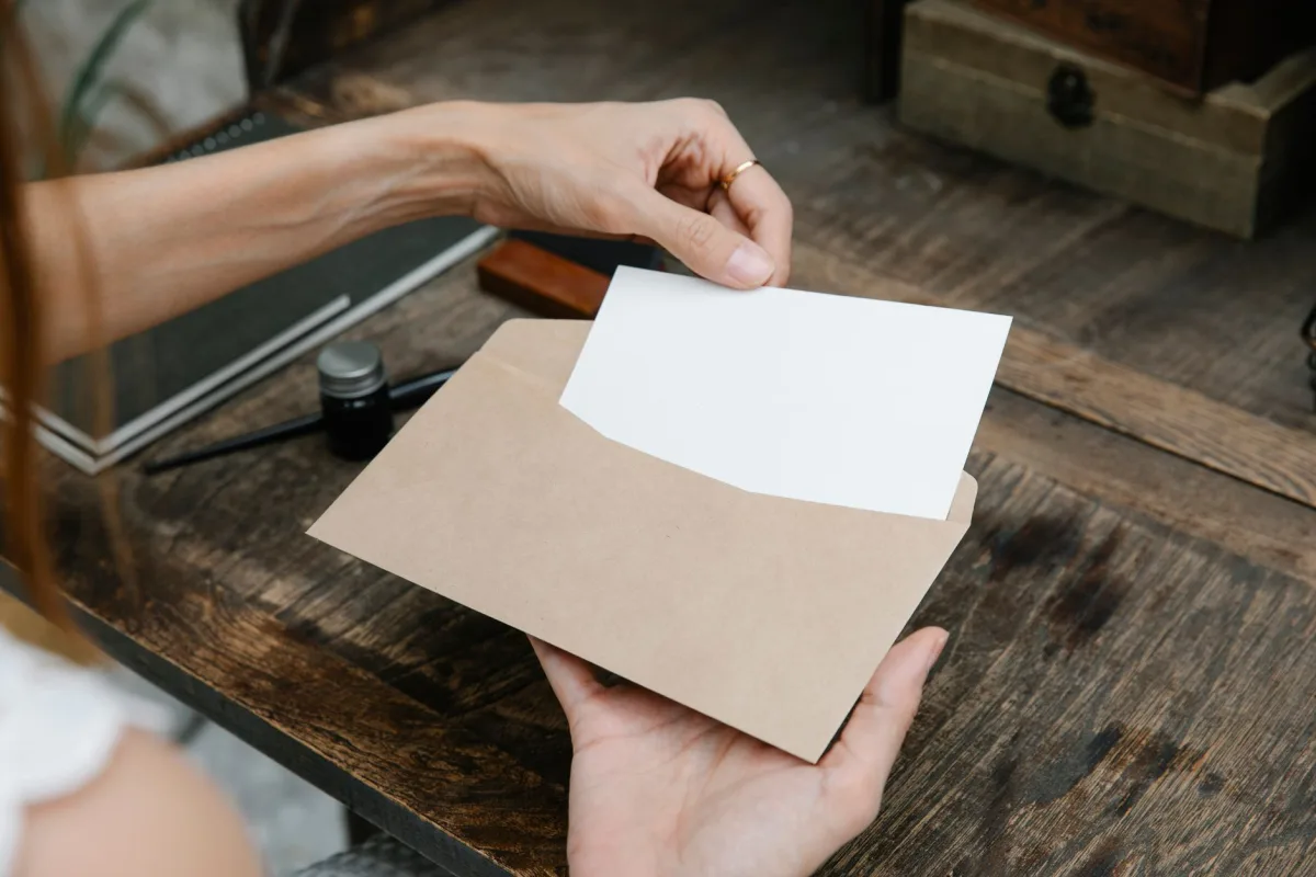 Close-up of hands holding an envelope with a letter on a rustic wooden desk, ideal for communication themes. Close-up of hands holding an envelope with a letter on a rustic wooden desk, ideal for communication themes.