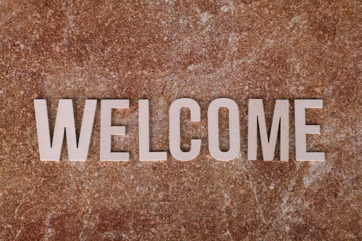 Close-up of a wooden 'Welcome' sign on a textured stone background. Close-up of a wooden 'Welcome' sign on a textured stone background.