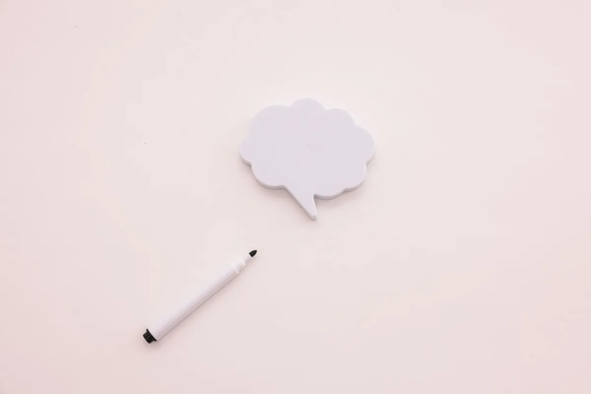 Minimalist image of a speech bubble and marker on a white background, ideal for creative concepts.