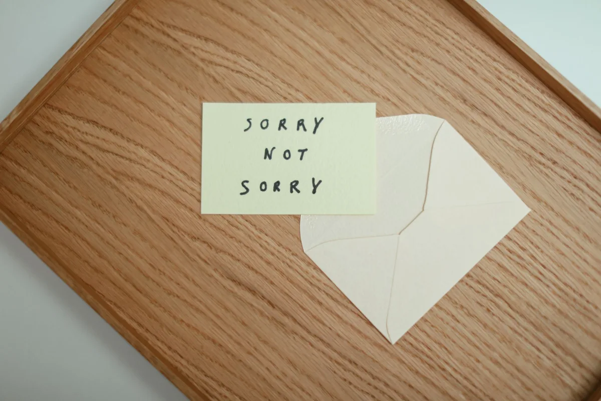 A flat lay of a 'Sorry Not Sorry' card with an envelope on a wooden surface. A flat lay of a 'Sorry Not Sorry' card with an envelope on a wooden surface.