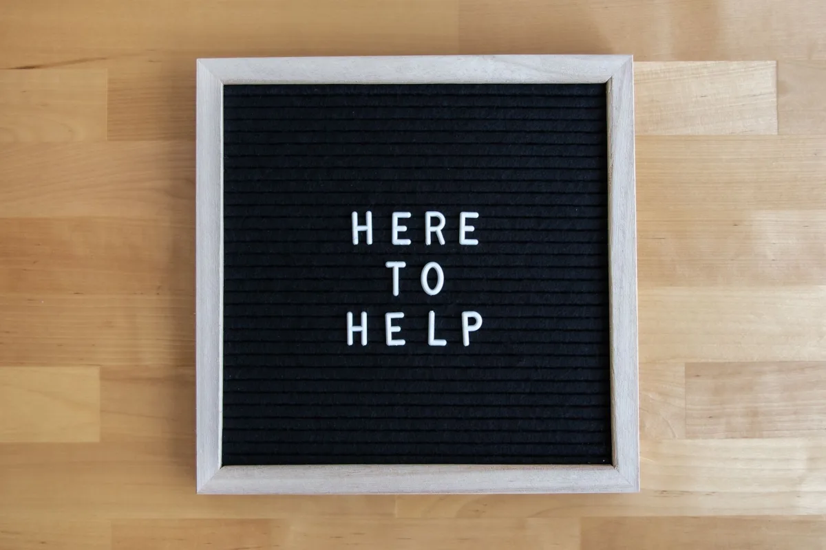 Black letter board with white text 'Here Help' on a wooden background. Black letter board with white text 'Here Help' on a wooden background.