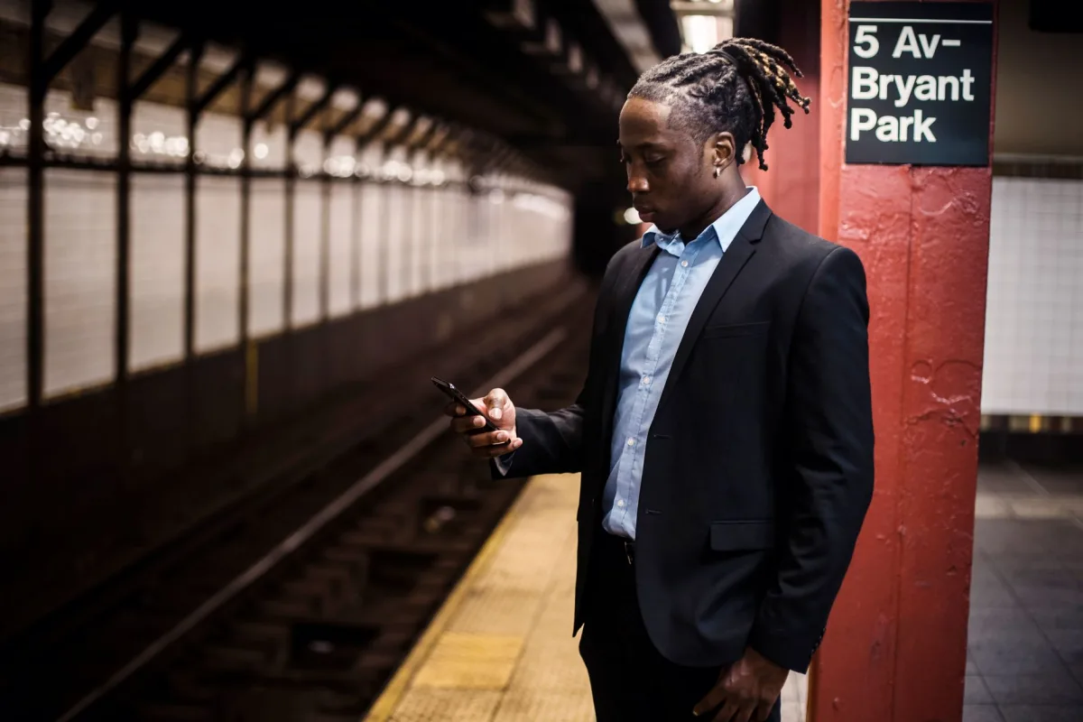 Modern young African American man in office suit text messaging on cellphone while waiting for train at Manhattan subway station Modern young African American man in office suit text messaging on cellphone while waiting for train at Manhattan subway station
