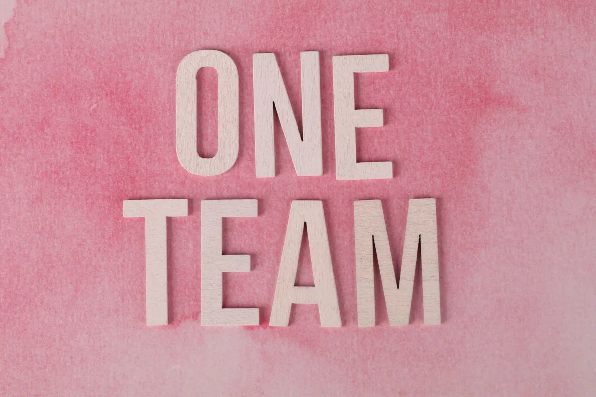 Wooden letters spelling 'One Team' on a pink textured background symbolizing unity.