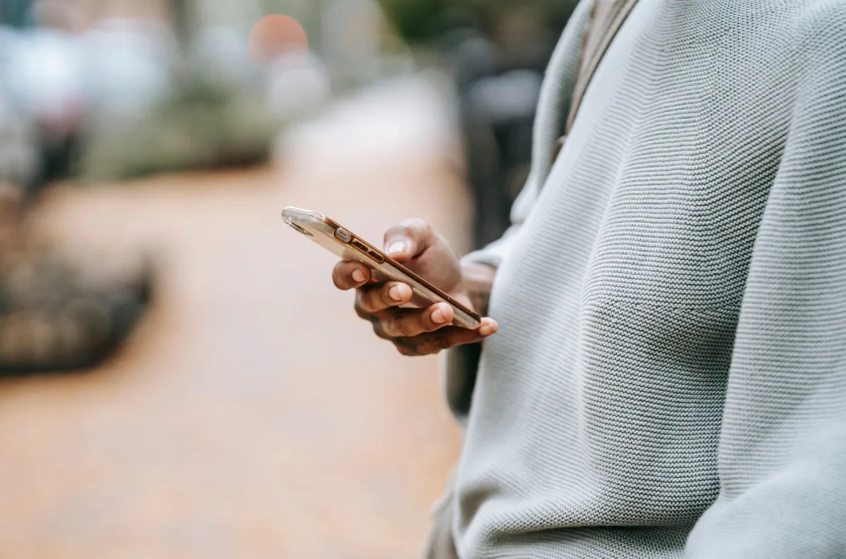 Crop unrecognizable female holding modern smartphone and messaging while standing on city street