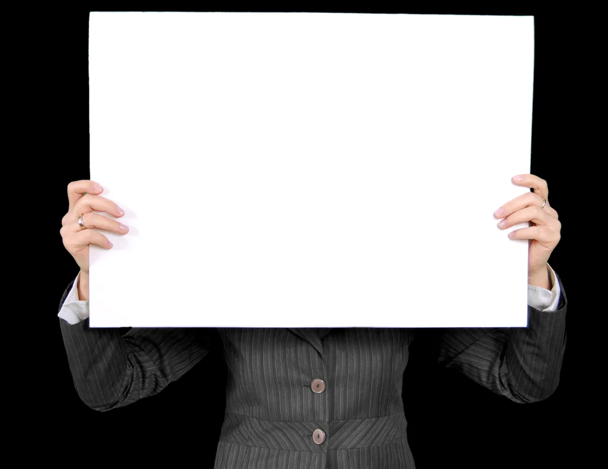 An individual in a formal blazer holds a blank whiteboard, ideal for custom messages.