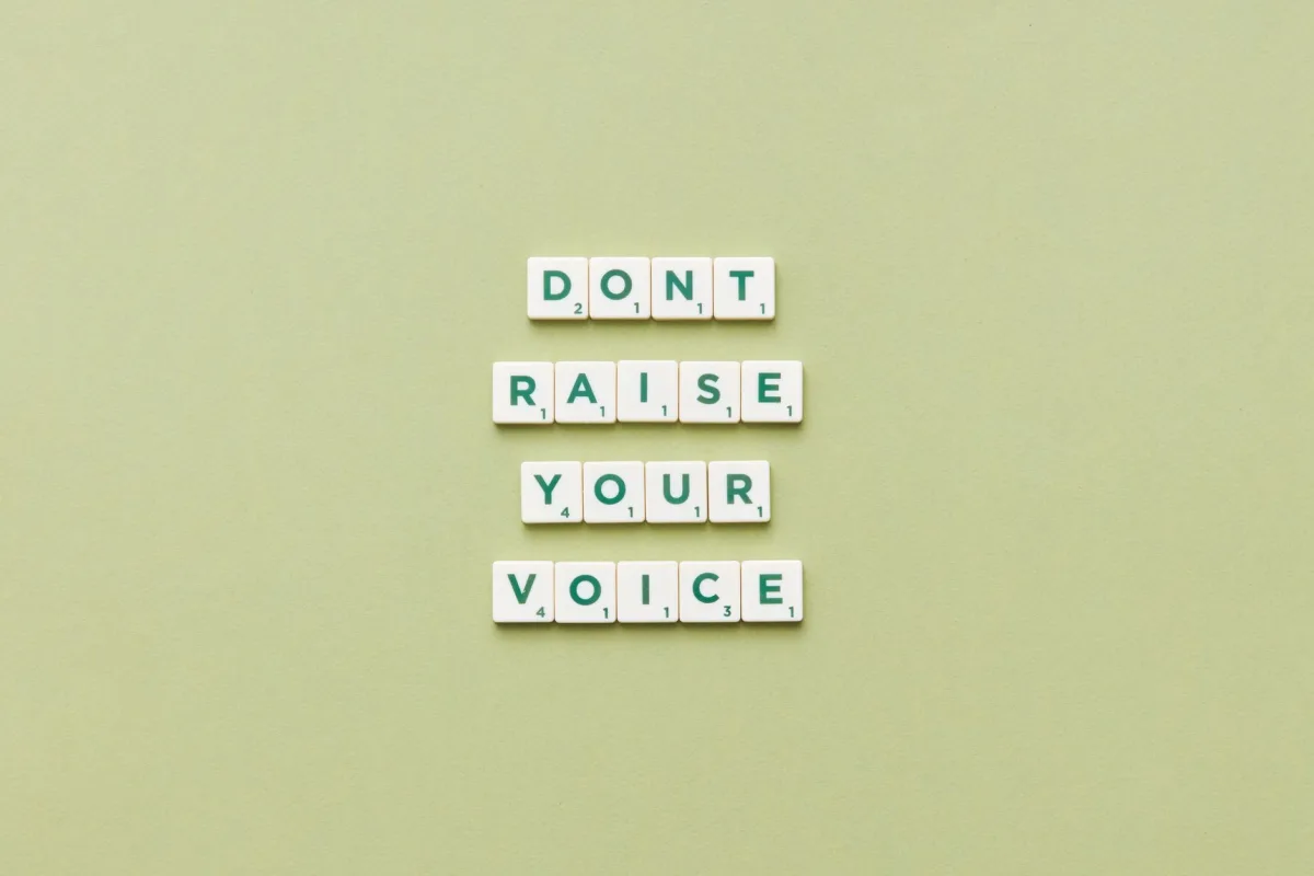 Scrabble tiles spelling 'Don't Raise Your Voice' on a green background.
