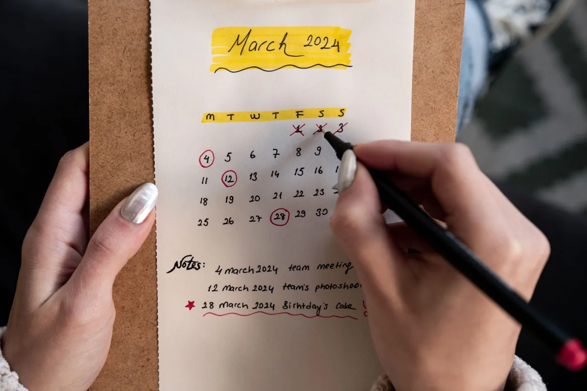 Close-up of a woman's hands organizing a planner for March 2024 with handwritten notes and highlights. Close-up of a woman's hands organizing a planner for March 2024 with handwritten notes and highlights.