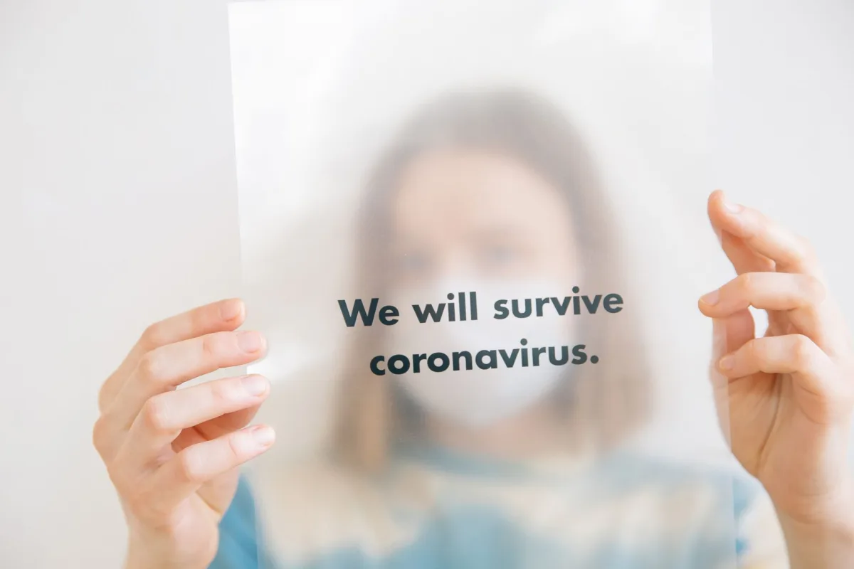 A person holds a sign saying 'We will survive coronavirus,' conveying hope during the pandemic.