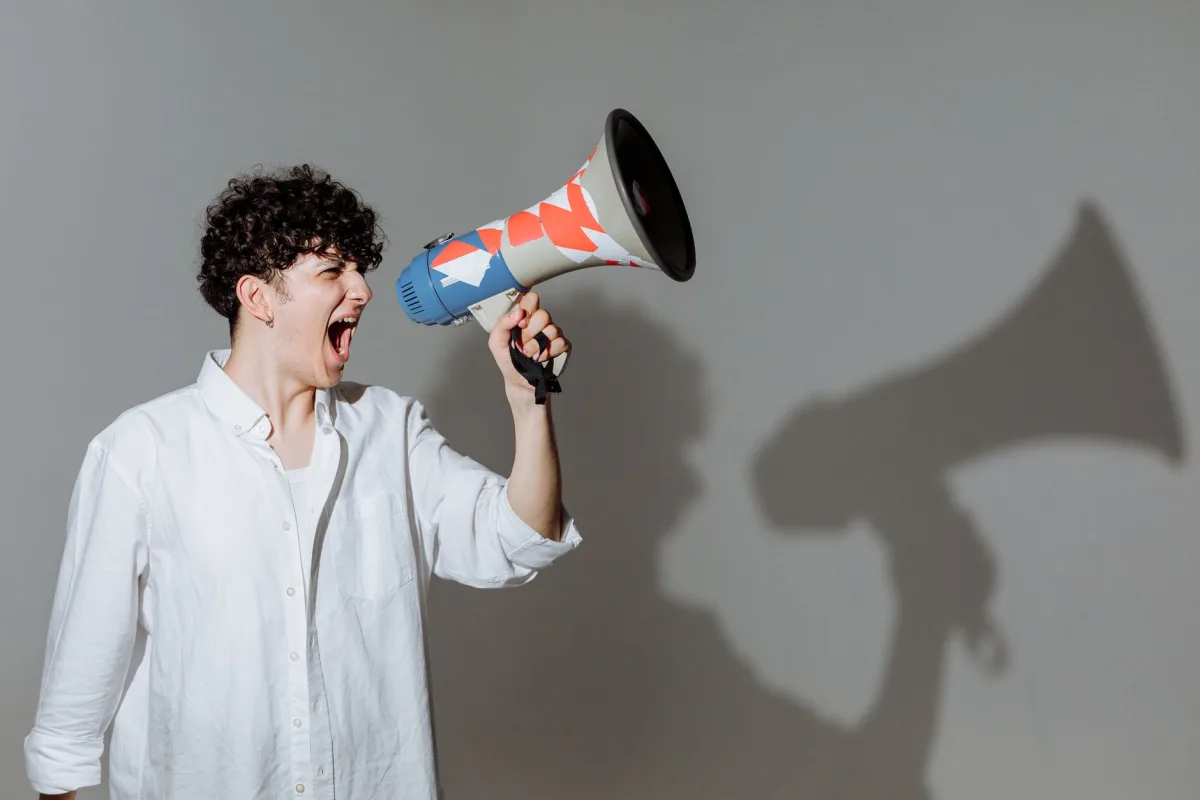 Young adult with curly hair energetically shouting through a colorful megaphone. Young adult with curly hair energetically shouting through a colorful megaphone.