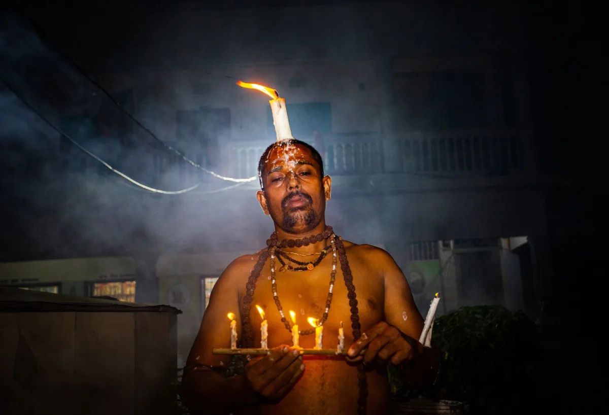A man participates in a traditional ritual, holding candles and adorned with fire.