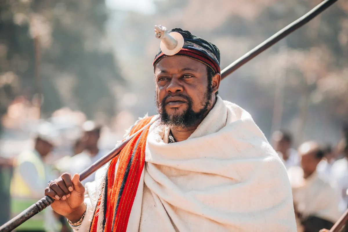 A man in traditional African attire holding a spear during a vibrant cultural festival outdoors.