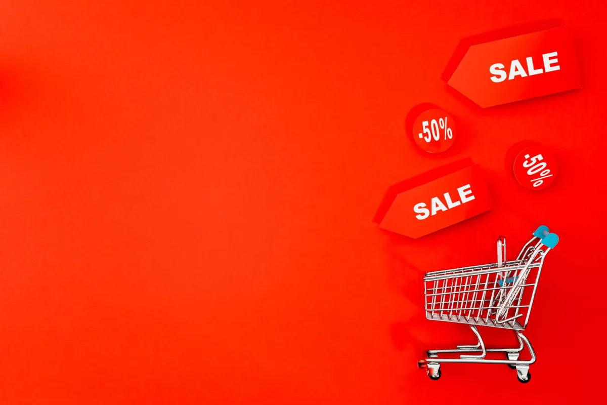 Shopping cart with sale tags on vibrant red backdrop promoting discounts. Shopping cart with sale tags on vibrant red backdrop promoting discounts.