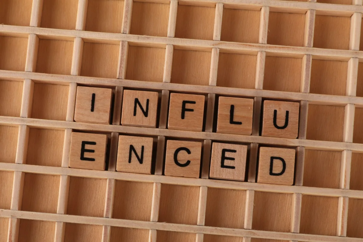Close-up of Scrabble tiles spelling 'influenced' arranged on a wooden grid layout. Close-up of Scrabble tiles spelling 'influenced' arranged on a wooden grid layout.