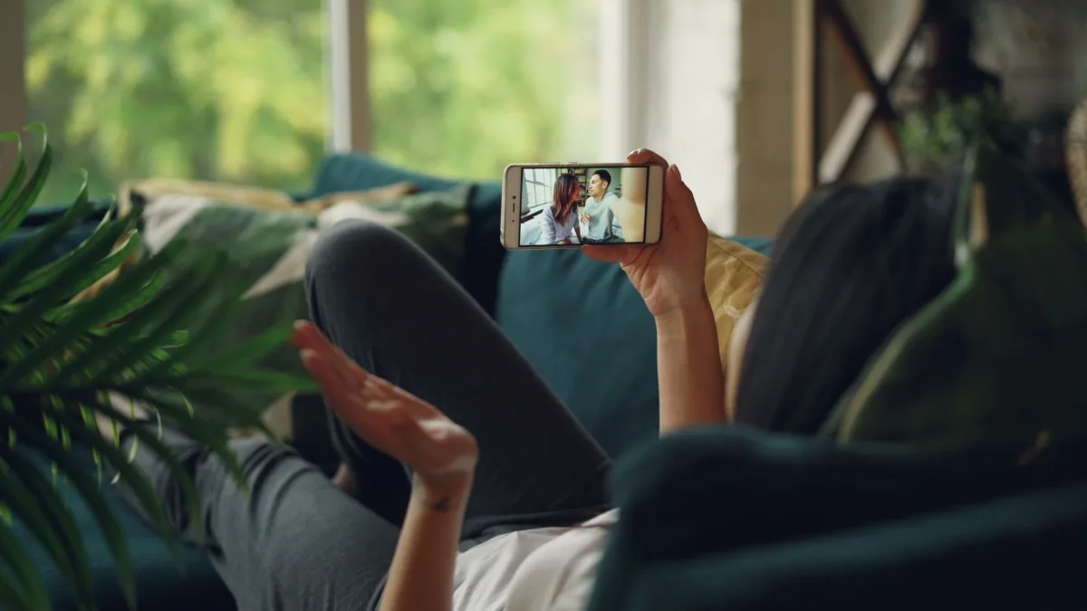 Woman relaxing on a couch, engaged in a video call on her smartphone, indoors. Woman relaxing on a couch, engaged in a video call on her smartphone, indoors.
