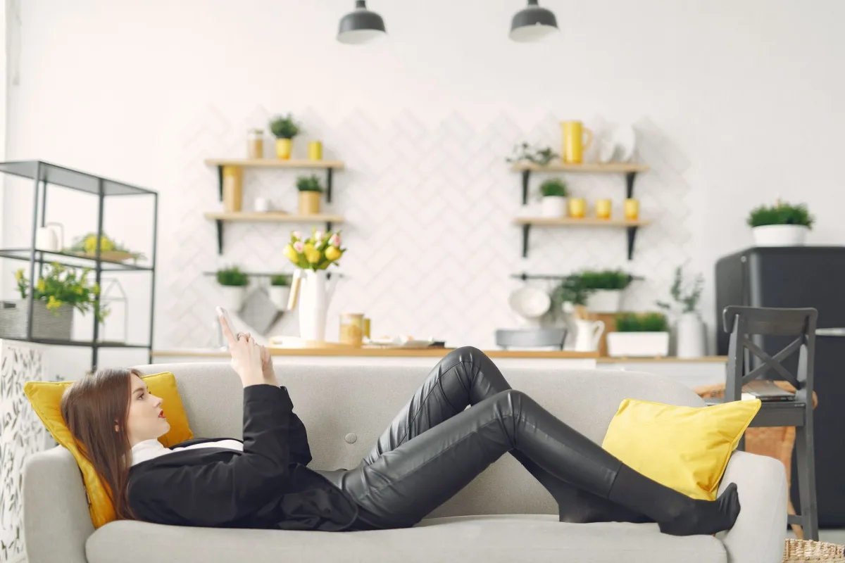 Side view of young female in trendy outfit relaxing on cozy couch in modern apartment and chatting in social media on mobile phone Side view of young female in trendy outfit relaxing on cozy couch in modern apartment and chatting in social media on mobile phone