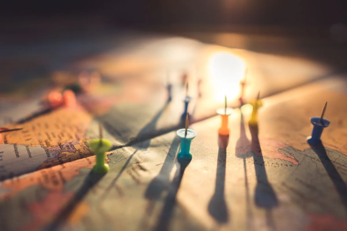 A close-up view of colorful push pins casting shadows on a world map during sunset, highlighting global travel. A close-up view of colorful push pins casting shadows on a world map during sunset, highlighting global travel.