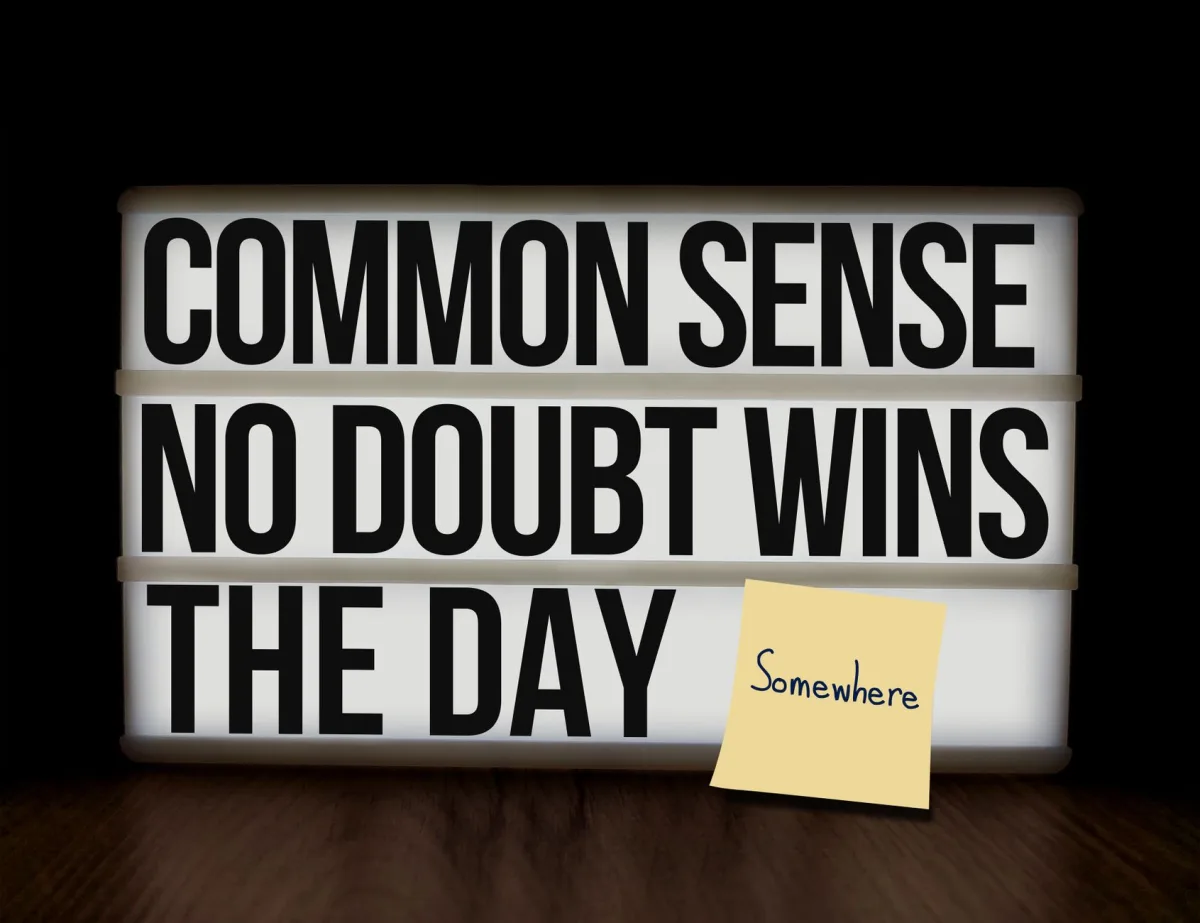 Lightbox with motivational quote 'Common Sense No Doubt Wins the Day' and sticky note on wood grain surface.