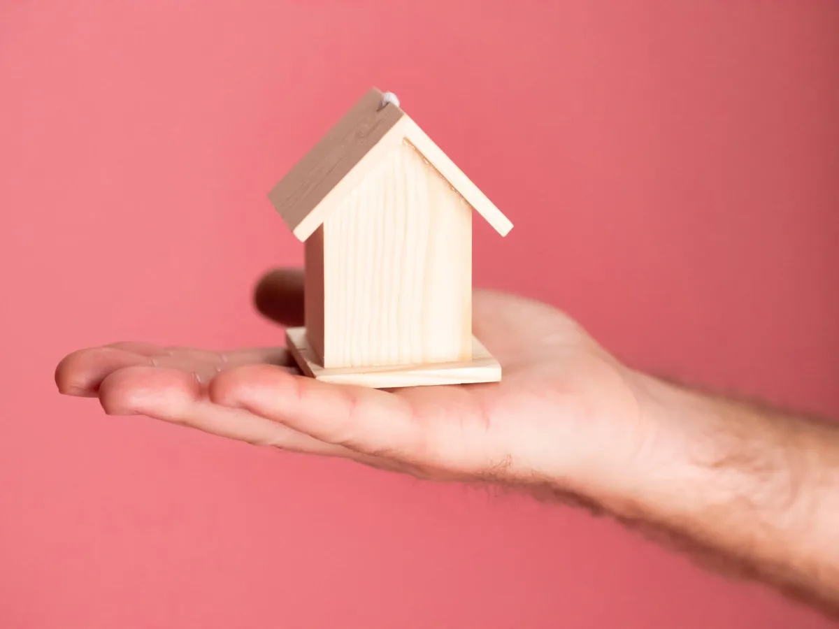 Wooden house model in hand symbolizing real estate concepts on pink background. Wooden house model in hand symbolizing real estate concepts on pink background.