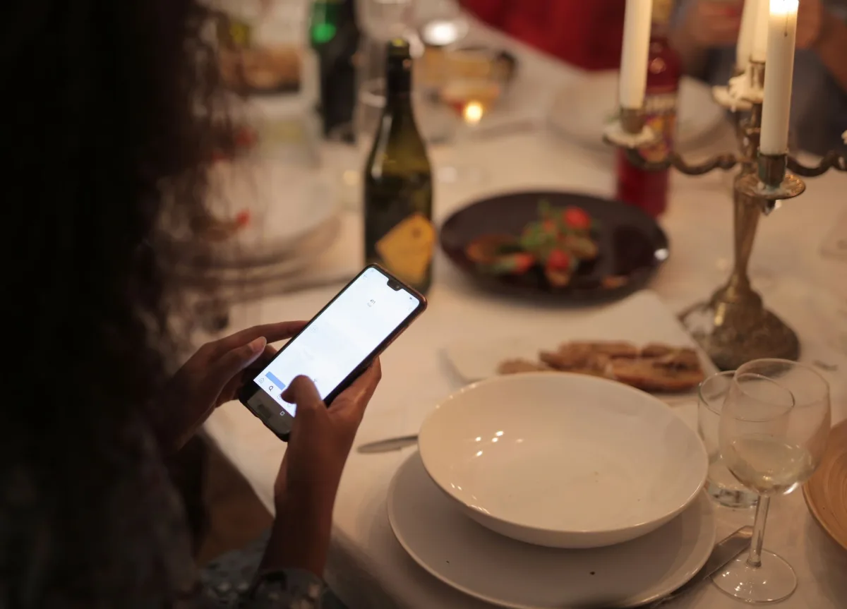 A cozy dinner setting with a woman using a smartphone at a candlelit table.