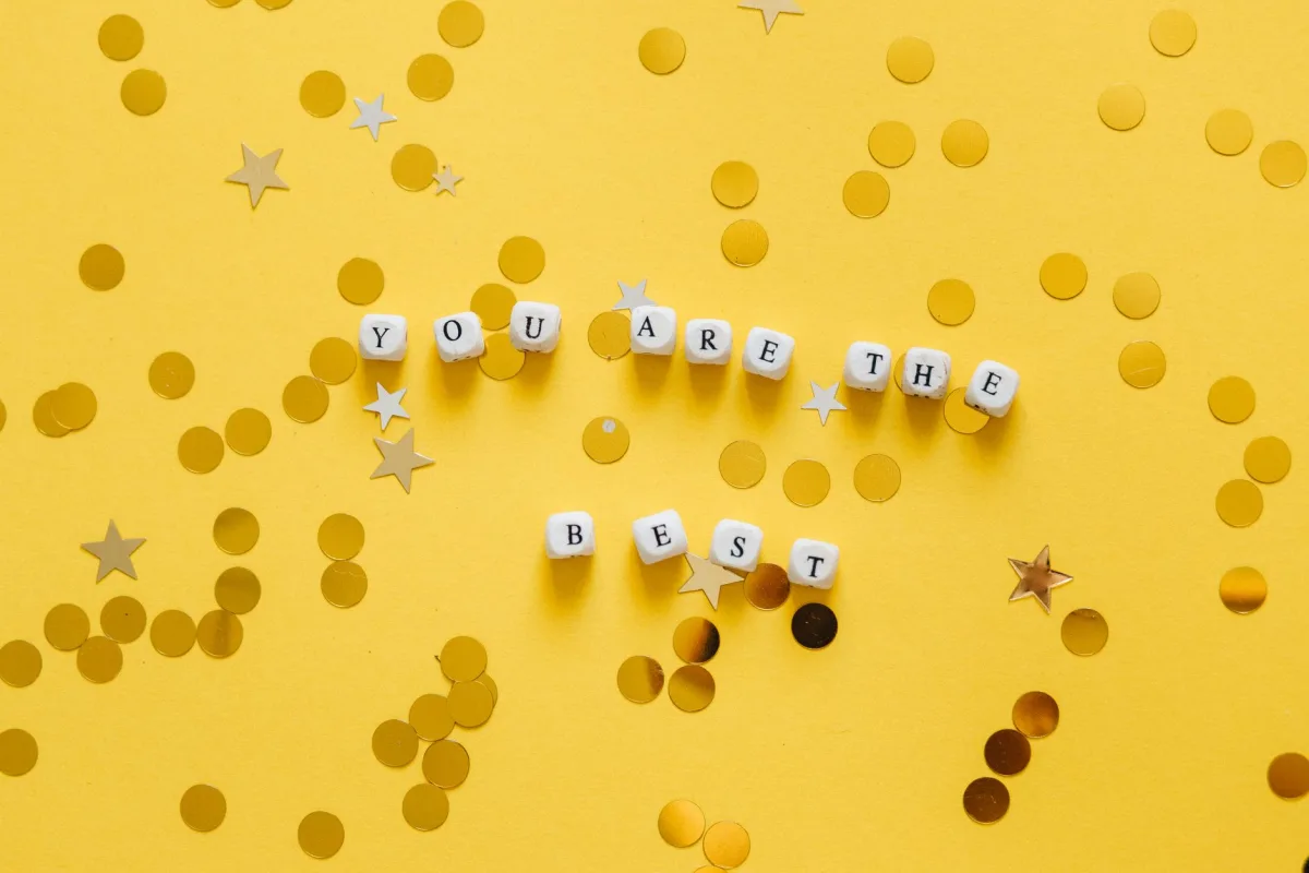 Inspirational message âYou Are the Bestâ spelled with dice on a vibrant yellow surface with star confetti. Inspirational message âYou Are the Bestâ spelled with dice on a vibrant yellow surface with star confetti.