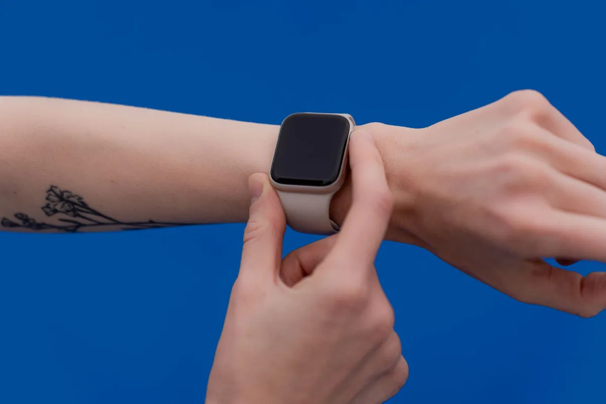 A person adjusting a modern smart watch against a bright blue background. A person adjusting a modern smart watch against a bright blue background.