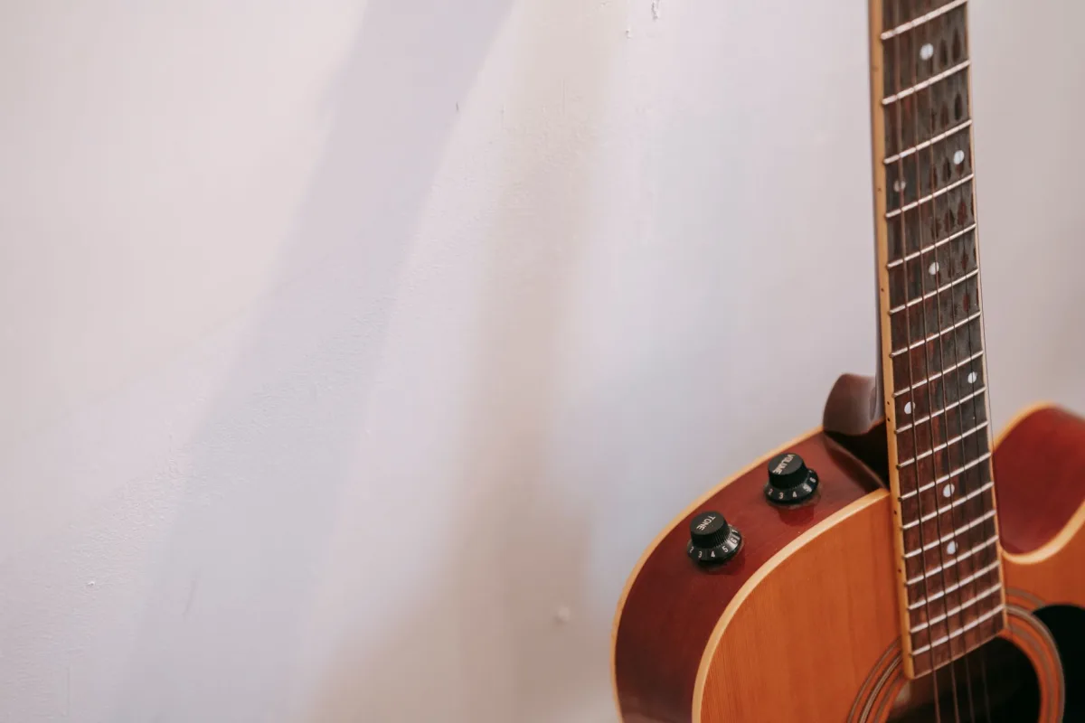 Detail of guitar neck with volume and tone knobs on body of brown musical instrument placed near white wall with shadow Detail of guitar neck with volume and tone knobs on body of brown musical instrument placed near white wall with shadow