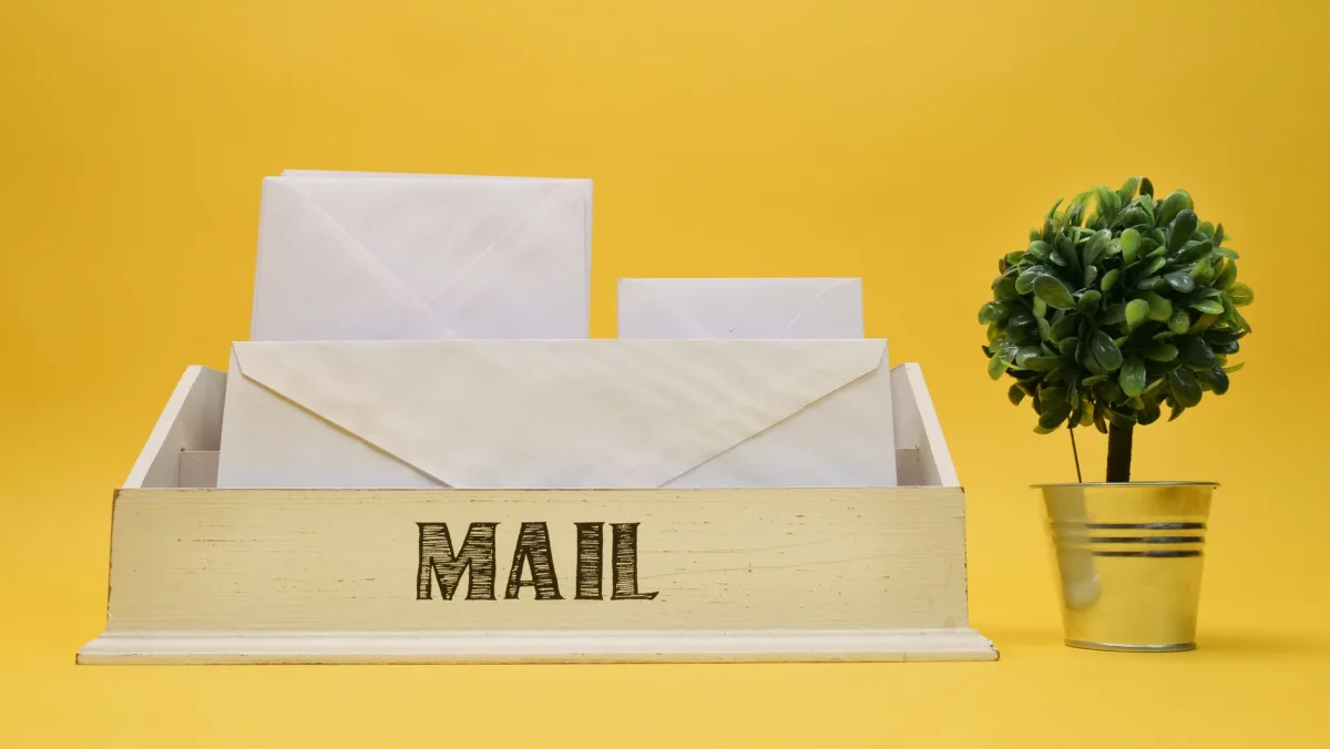 A wooden mail organizer with white envelopes and small potted plant on a yellow background. A wooden mail organizer with white envelopes and small potted plant on a yellow background.