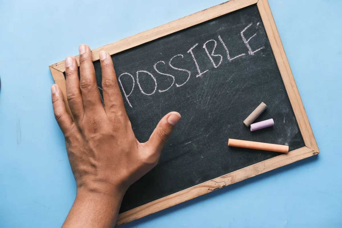 A hand on a chalkboard with 'Possible' written in chalk signifies optimism and potential. A hand on a chalkboard with 'Possible' written in chalk signifies optimism and potential.