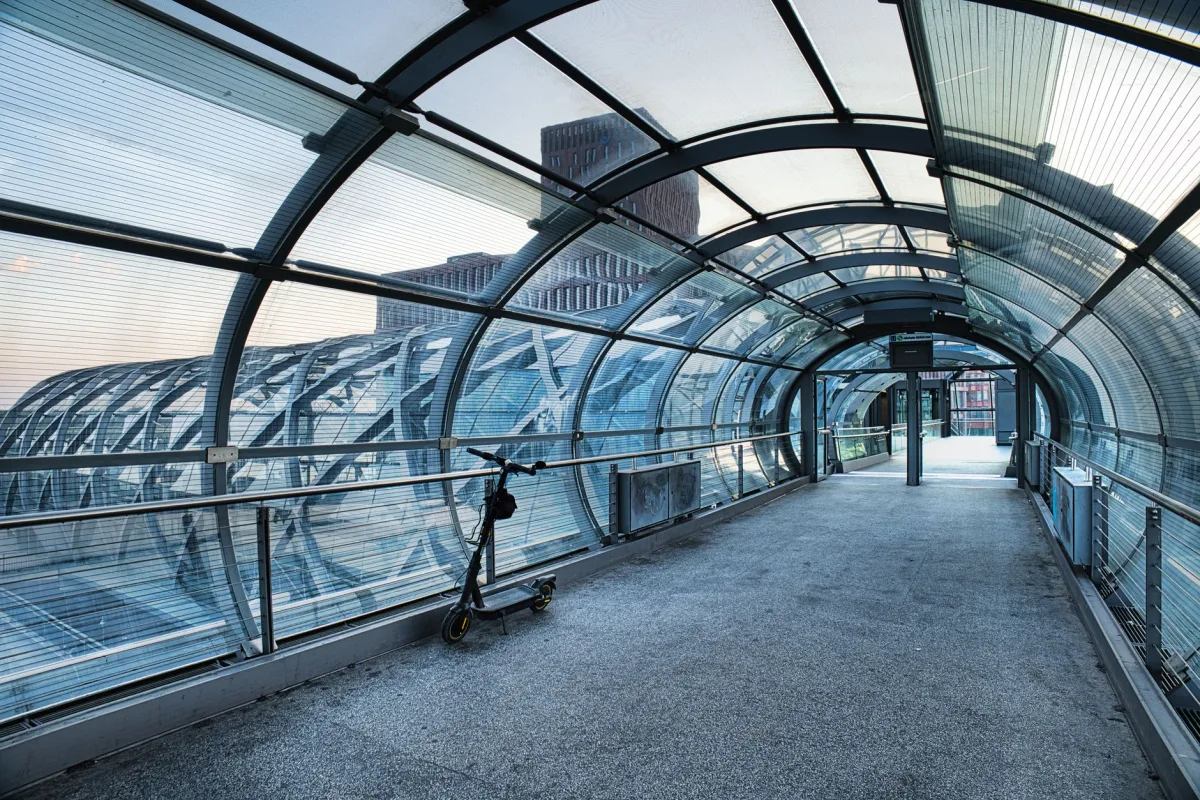 A sleek urban pedestrian tunnel featuring a parked scooter under a glass roof.