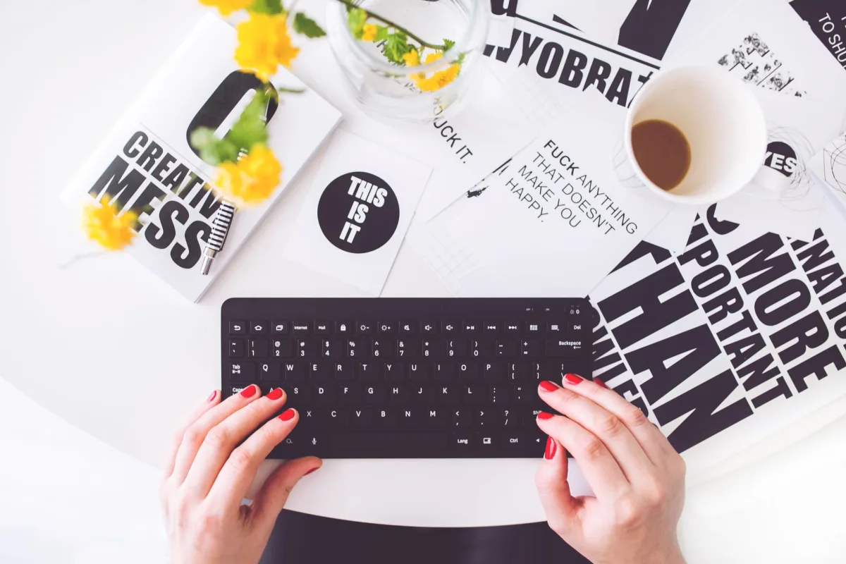A creative workspace featuring a woman typing with red nails, surrounded by inspirational typography.